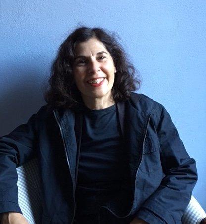 A woman with dark hair sitting in a chair with a blue background